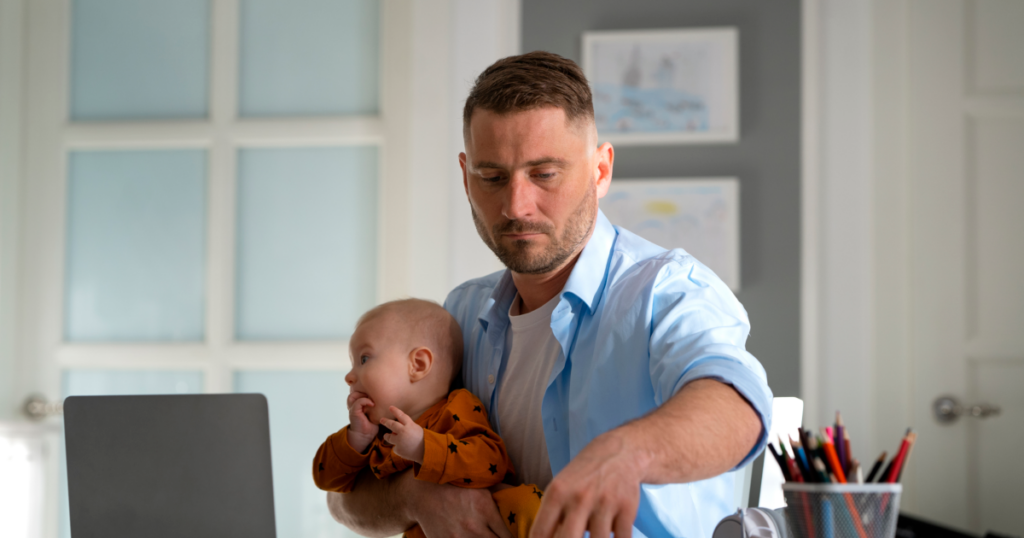 Vater mit Baby auf dem Arm arbeitet am Laptop
